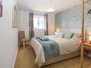 A bedroom with a bed covered with pillows and towels next to a window with patterned curtains at Beck View in Weston Longville near Lenwade