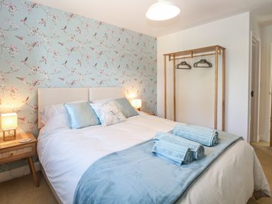 A bedroom with a bed lamps bedside tables a wooden clothes rack and floral wallpaper at Beck View in Weston Longville near Lenwade