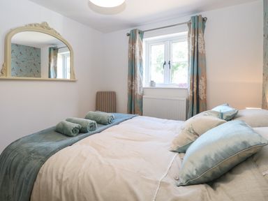 A bedroom with a bed pillows rolled towels a window with curtains and a wall mirror at Beck View in Weston Longville near Lenwade