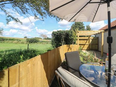 An outdoor patio area with a table and chairs under an umbrella a wooden fence and garden at Beck View in Weston Longville near Lenwade