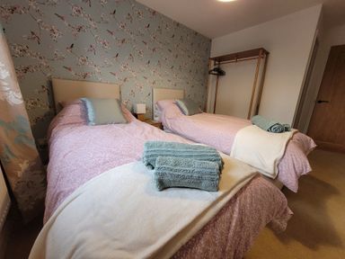 A bedroom with two single beds with pink bedding and blue cushions and folded towels on a white blanket at Beck View in Weston Longville near Lenwade
