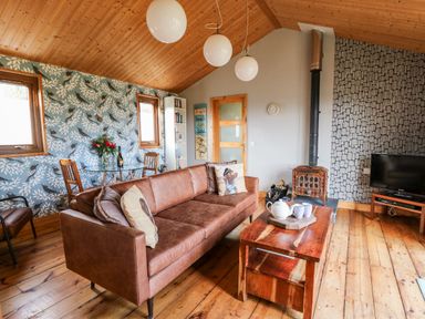 A living room with a brown leather sofa wooden coffee table and a wood burning stove at Y Caban Glas in Rhydlewis near Brynhoffnant