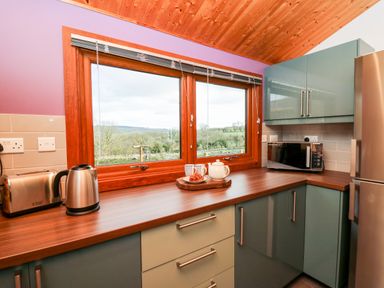 A kitchen countertop with a toaster kettle teapot cups and a microwave by a window at Y Caban Glas in Rhydlewis near Brynhoffnant