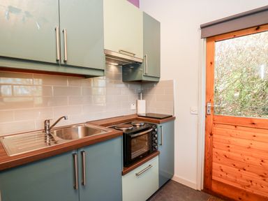A kitchen with teal cabinets wooden countertops a sink an oven and a wooden door with glass at Y Caban Glas Rhydlewis near Brynhoffnant