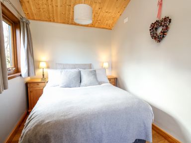 A bedroom with a double bed two bedside tables with lamps a window and a heart-shaped decoration on the wall at Y Caban Glas in Rhydlewis near Brynhoffnant