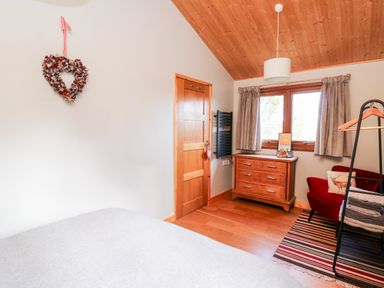 A bedroom with wooden ceiling wooden floor a wooden dresser and a red chair with a pillow at Y Caban Glas Rhydlewis near Brynhoffnant