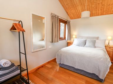 A bedroom with a bed beside two wooden nightstands with lamps and a window with curtains at Y Caban Glas in Rhydlewis near Brynhoffnant