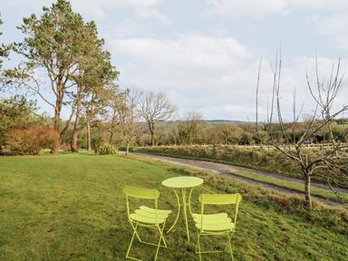A garden area with two green chairs and a table on grass near trees and a gravel path at Y Caban Glas in Rhydlewis near Brynhoffnant