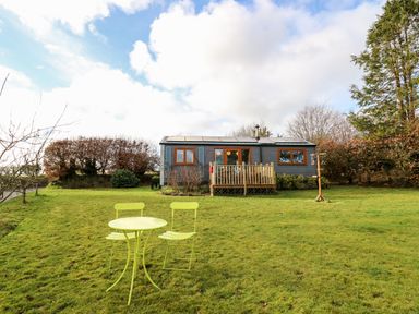 A small house with a deck and a green table with two chairs on a lawn at Y Caban Glas in Rhydlewis near Brynhoffnant