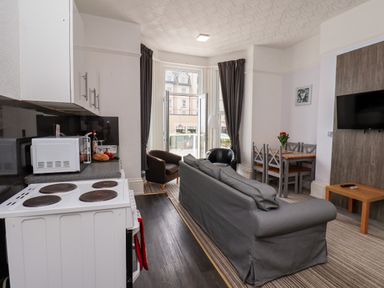 A kitchen with a stove and microwave next to a living area with a sofa chairs dining table and wall mounted television at Beach in Bridlington