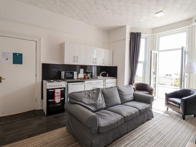 A living room with a gray sofa two armchairs kitchenette and a door to a balcony at Beach in Bridlington