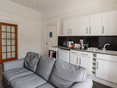 A kitchen with white cabinets a countertop appliances and a gray sofa in front at Beach in Bridlington
