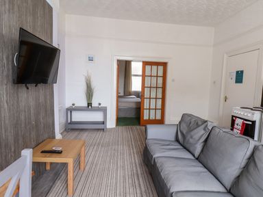 A living room with a grey couch a wall-mounted TV a small wooden table and a side table with plants at Beach Bridlington