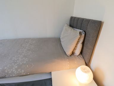 A bed with grey headboard and beige patterned bedding next to a white nightstand with a lit lamp at Beach in Bridlington
