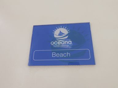 A blue sign with a sun and boat logo and the text Oceana holiday lettings Beach