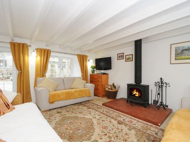 A living room with sofas yellow curtains a television and a wood burning stove at Henwood Barn in Henwood near Upton Cross