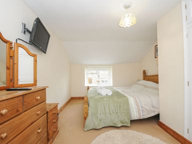 A bedroom with a wooden bed with folded towels on the bed a wooden dresser with a mirror a wall-mounted TV and a small window at Henwood Barn in Henwood near Upton Cross