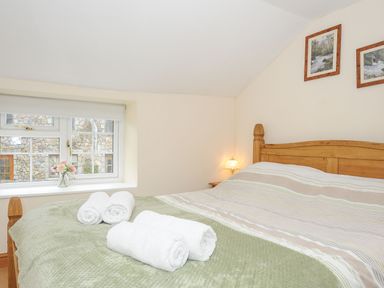 A bedroom with a wooden bed frame towels on the bed and framed pictures on the wall at Henwood Barn in Henwood near Upton Cross