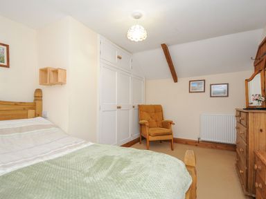 A bedroom with a bed a wooden chair built in wardrobe and a wooden dresser with a mirror at Henwood Barn in Henwood near Upton Cross