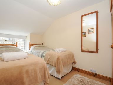 A bedroom with two single beds covered with beige and striped bedding a wall mirror and a window at Henwood Barn Henwood near Upton Cross
