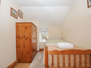 A small bedroom with a single wooden bed with folded towels on it a wooden wardrobe and a window at Henwood Barn Henwood near Upton Cross