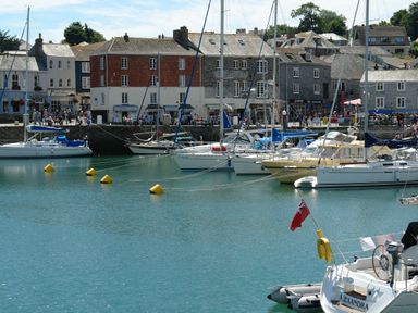 A harbor with sailboats docked and buildings with people walking along the waterfront Henwood Barn Henwood near Upton Cross