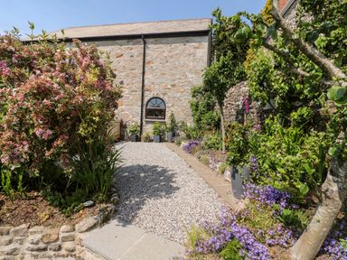 A garden with gravel pathway stone wall flowering plants and trees at Henwood Barn in Henwood near Upton Cross