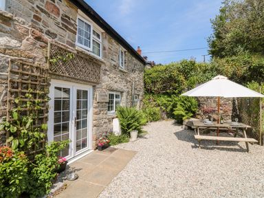 A stone house exterior with white doors and windows a gravel patio with a wooden picnic table and a white umbrella at Henwood Barn in Henwood near Upton Cross