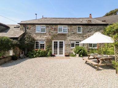 A stone cottage with multiple windows gravel yard and a wooden picnic table with umbrella at Henwood Barn Henwood near Upton Cross
