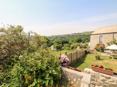 A garden with flowering plants and a stone building with a wooden fence at Henwood Barn Henwood near Upton Cross