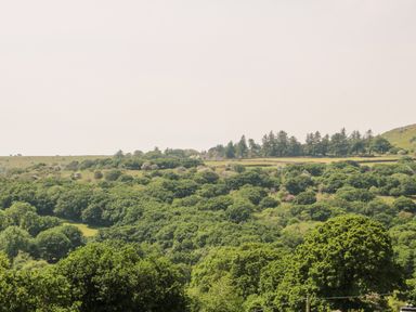 A landscape with dense green trees and a few buildings in the distance at Henwood Barn in Henwood near Upton Cross