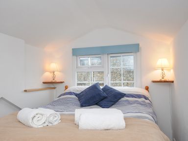 A bedroom with a double bed with striped bedding two blue pillows two bedside lamps and three rolled towels on the bed at Mole Cottage in Henwood near Upton Cross