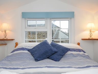 A bedroom with a bed with blue striped bedding and two blue pillows with lamps on wooden shelves on either side at Mole Cottage in Henwood near Upton Cross