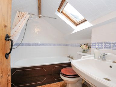 A bathroom with a bathtub with shower curtain a toilet with wooden seat a sink and a skylight window at Mole Cottage Henwood near Upton Cross