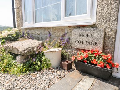 A stone wall with a window and a sign that says Mole Cottage with flowers and a stone slab at Mole Cottage in Henwood near Upton Cross