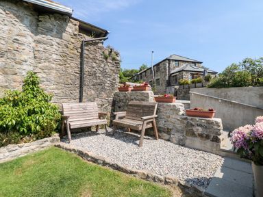 An outdoor sitting area with two wooden benches and flower pots on stone walls at Mole Cottage Henwood near Upton Cross