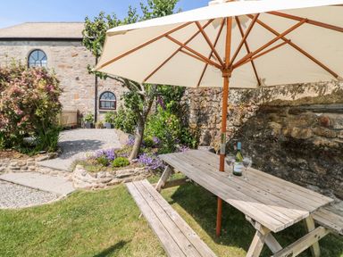A garden picnic table with umbrella and wine glasses near a stone wall and a stone building at Mole Cottage in Henwood near Upton Cross