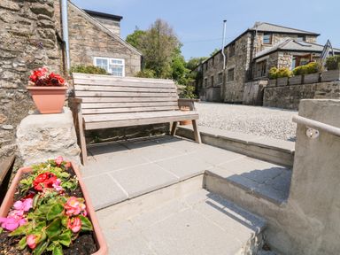 An outdoor patio area with a wooden bench and flower pots near stone buildings at Mole Cottage in Henwood near Upton Cross