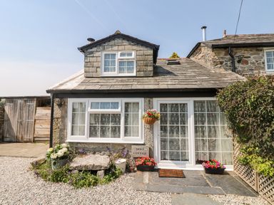 The exterior of a stone cottage with white framed windows and a door with flower pots outside at Mole Cottage in Henwood near Upton Cross