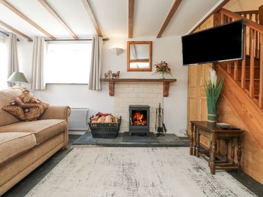 A living room with a sofa a fireplace with firewood a wall-mounted television and a wooden staircase at Mole Cottage in Henwood near Upton Cross