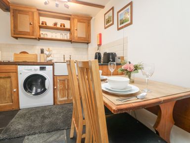 A kitchen with wooden cabinets a washing machine a dining table with bowls and glasses and chairs at Mole Cottage in Henwood near Upton Cross