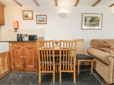A dining area with wooden chairs and table set with plates next to a kitchen counter and sofa at Mole Cottage Henwood near Upton Cross