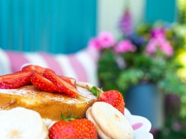 A plate with a pancake topped with sliced strawberries and whole strawberries and cookies in an outdoor setting with flowers in the background