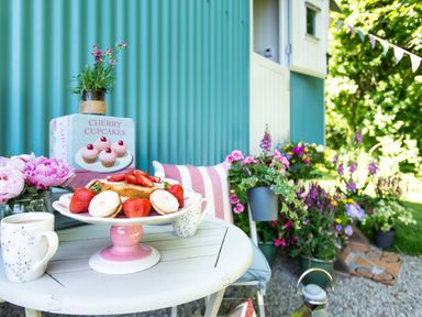 A table with a cake and strawberries cups of tea and flowers outside a hut with plants and cushions at Gwithian Shepherds Hut in Angarrack near Hayle