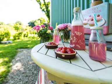 A garden table with two strawberry tarts two bottles of pink drink and pink flowers at Gwithian Shepherds Hut Angarrack near Hayle