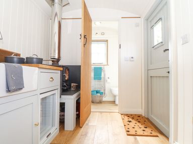 A small kitchen area with a stove sink and pots next to a wooden door leading to a bathroom with a towel rack and toilet at Gwithian Shepherds Hut Angarrack near Hayle