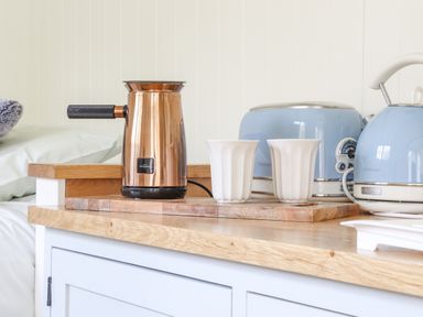 A wooden countertop with a copper milk frother two white cups a blue toaster and a blue kettle at Gwithian Shepherds Hut in Angarrack near Hayle