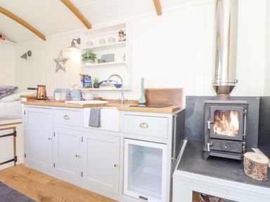 A kitchen area with light blue cabinets a wood countertop a sink a small stove a wood burning stove and a small refrigerator at Gwithian Shepherds Hut in Angarrack near Hayle