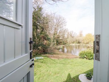 View through an open door showing a grassy garden area with a pond and trees at Gwithian Shepherds Hut in Angarrack near Hayle