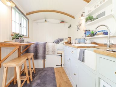 A small kitchen and sleeping area with wooden stools and a bed at Gwithian Shepherds Hut in Angarrack near Hayle
